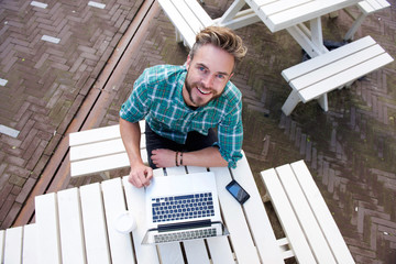 Smiling man sitting outside with laptop from above