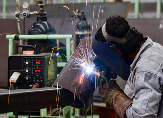 Welder in factory with protective equipment welding pipe
