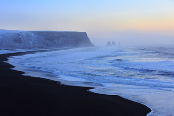 Landscape with beach of black sand and   the sea stacks in the background at sunrise. Reynisdrangar , near Vik, Iceland