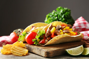 Homemade tasty burrito with vegetables and potato chips on cutting board, on dark background