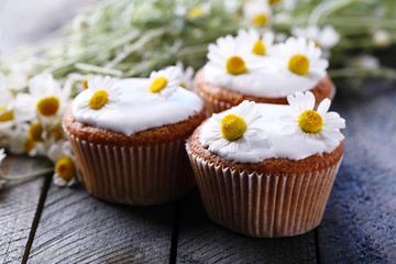 Chamomile flowers and tasty muffins on color wooden background