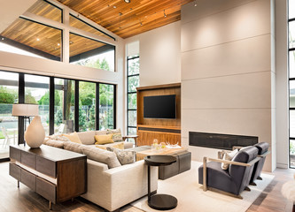 Obraz premium Beautiful living room interior in luxury home with hardwood floors, vaulted ceiling, large bank of windows with view of lush vegetation