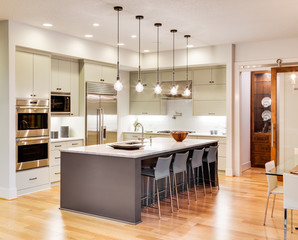 Beautiful kitchen interior with island, sink, stainless steel appliances, hardwood floor, and pendant lights in new luxury home