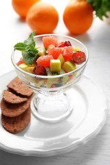 Fruit salad in glass bowl, on light wooden background
