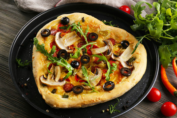 Heart shaped pizza on metal tray on wooden background