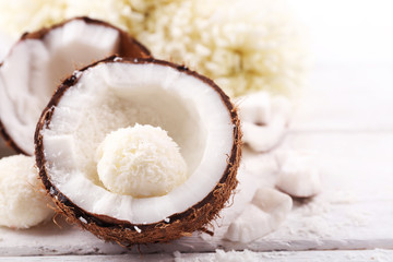 Candies in coconut flakes and fresh coconut on  light wooden background