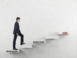 An ambitious man in a suit is going up the corporate ladder from the manager to CEO. Concrete background.