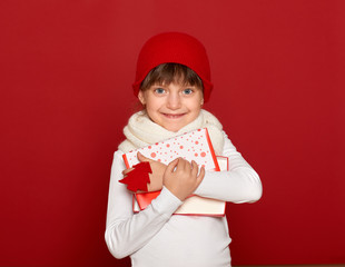 winter, child,  christmas concept - happy girl in hat with box gift show fir tree wool toy on red