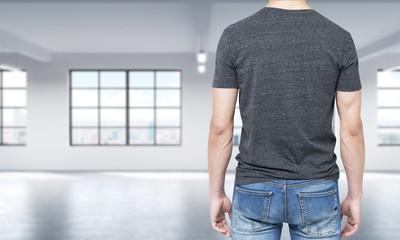 Rear view of the man in grey t-shirt and denims. Modern loft style open space on the background.