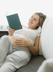 happy pregnant woman reading book on sofa