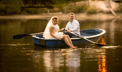 happy bride and groom sitting in wooden rowing boat at sunset
