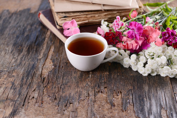 Old books with beautiful flowers and cup of tea on wooden table close up