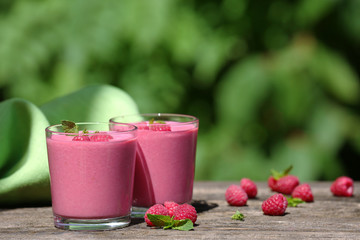 Glasses of raspberry milk shake with berries on bright background