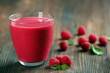 Glass of raspberry milk shake with berries on wooden table close up