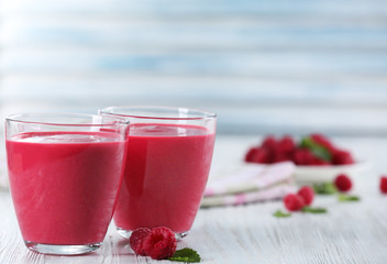 Glasses of raspberry milk shake with berries on wooden table close up