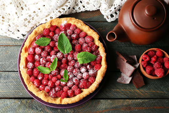 Tart with fresh raspberries and teapot, on wooden background