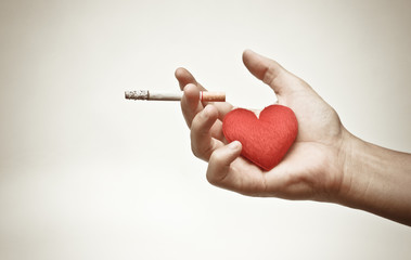 male hand holding a cigarette with a red heart / making to right decision about smoking concept