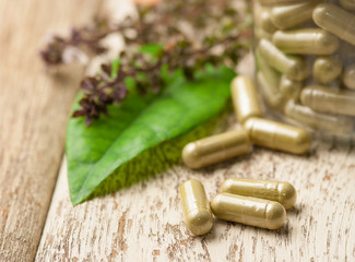 Herb capsule with green herbal leaf on wood