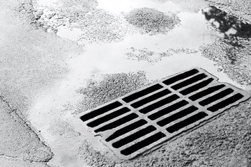 sewer grate on wet road with puddles