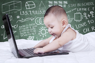 Baby playing laptop on bed with doodles background