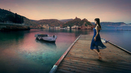 Fairy woman in dress on the dock by the sea on a background of mountains.