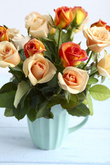 Bouquet of orange roses in cup on blue wooden background