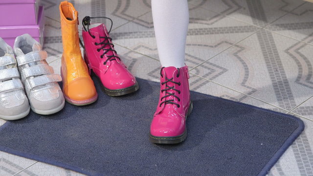 Child chooses footwear in shoe store for kids tries on new colorful boots closeup