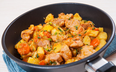 stewed meat with potatoes, onion and carrot in a frying pan