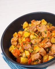stewed meat with potatoes, onion and carrot in a frying pan