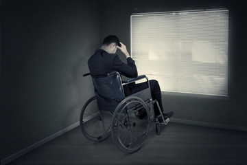 Stressful man sitting on the wheelchair near the window