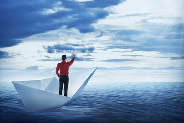 Obraz premium Asian business man pointing the sky, standing on the paper boat