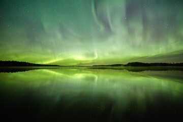Northern lights on the night sky.Green light reflection on the water of a lake.