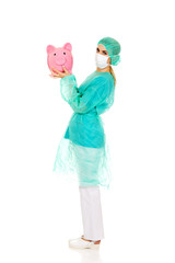 Female surgeon doctor holding piggy bank