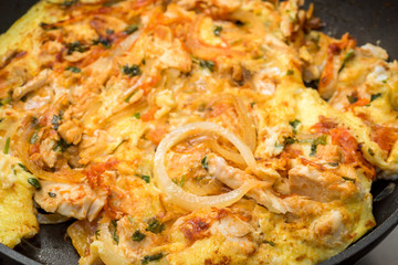 close up of cooking omelette with onion, tomatoes, chicken and parsley on a frying pan