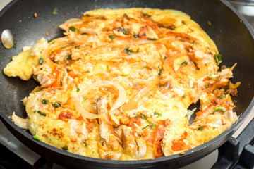close up of cooking omelette with onion, tomatoes, chicken and parsley on a frying pan