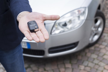 man hand with car in background holding a automobile key