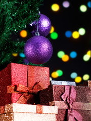 Christmas baubles hanging on tree branches in front of presents, on black background.