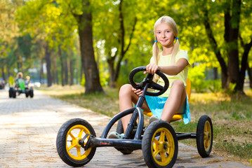 Beautiful smiling little girl riding toy car in summer city park