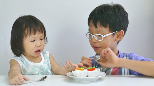 Asian siblings eating cake together in living room 

