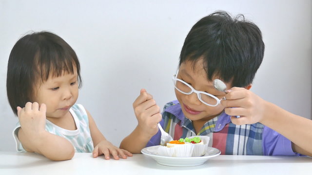 Asian siblings eating cake together in living room 

