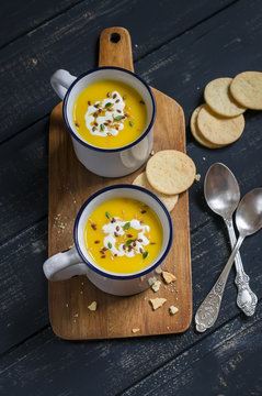 pumpkin soup in ceramic mugs on a wooden surface - healthy food