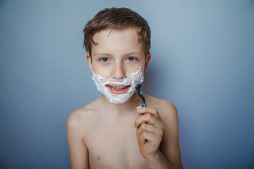 Boy  teenager European appearance   shaves face on a gray