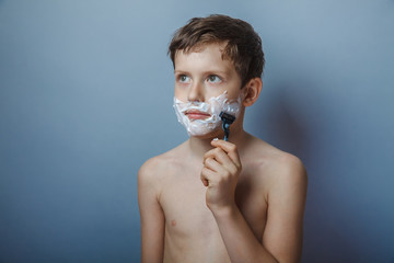 Boy  teenager European appearance shaves face on a gray 