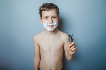 Boy  teenager European appearance  shaves face on a gray 