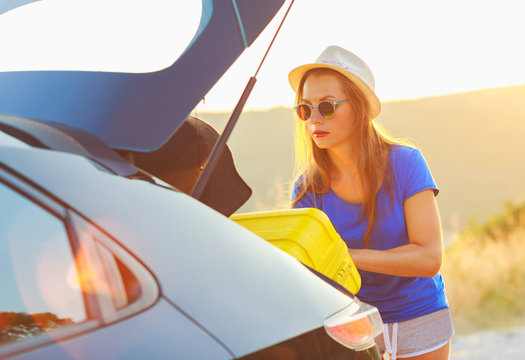 Woman loading luggage into the back of car parked alongside the