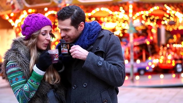 Paar isst S&uuml;&szlig;igkeiten auf Weihnachtsmarkt vor dem festlich beleuchteten Karussell 