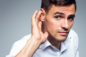 Young businessman holds his hand near ear.Close up portrait - obrazy, fototapety, plakaty