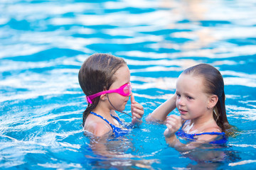 Adorable little girls playing in outdoor swimming pool on
