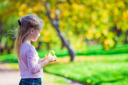 Adorable little girl with apple outdoors at beautiful autumn