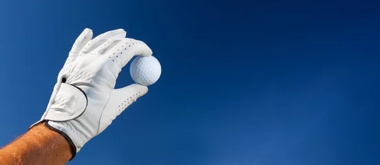 Papier Peint photo Golf Main portant un gant de golf tenant une balle de golf blanche - grand espace de copie sur la droite